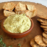 bowl of edamame dip on a round wood board surrounded by crackers