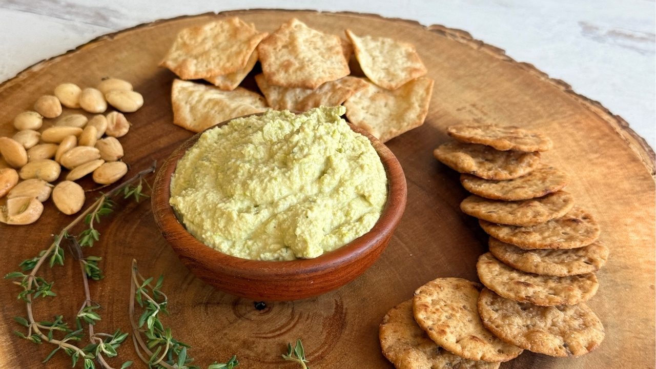 bowl of edamame dip on a round wood board surrounded by crackers