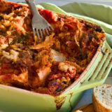 green casserole dish with a baked lasagna inside next to slices of bread