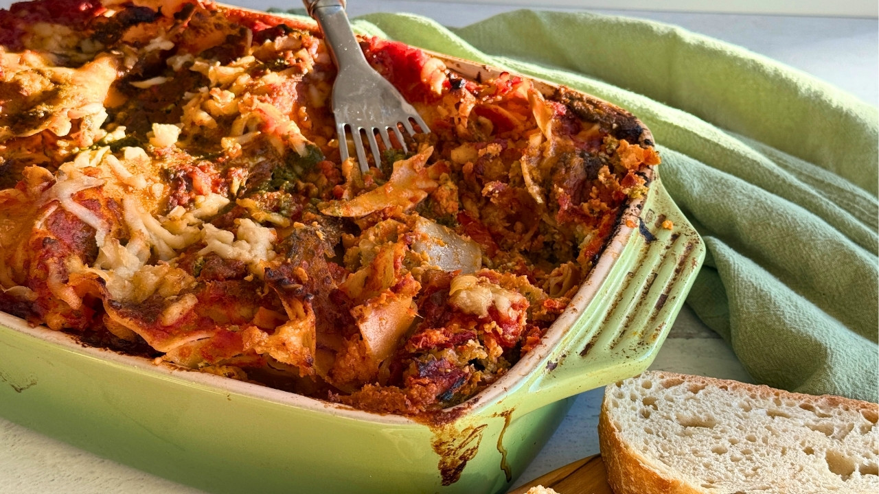 green casserole dish with a baked lasagna inside next to slices of bread