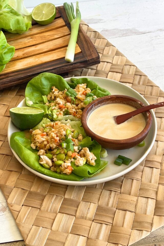 plate of lettuce wraps alongside a small wooden bowl of sauce with a spoon in it