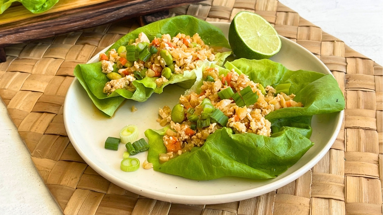 Lettuce wraps on a white plate on top of a wicker placemat