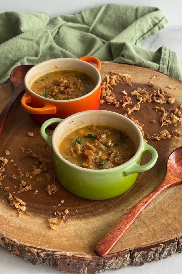 two bowls of soup on a wooden board surrounded by fried onions