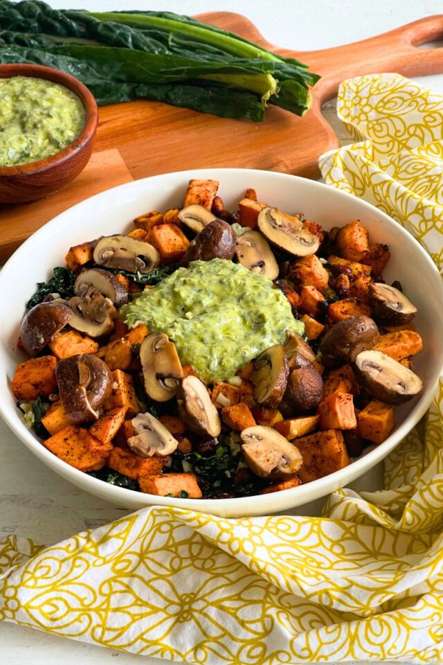 bowl of sweet potatoes and mushrooms in front of a wood cutting board with kale on it