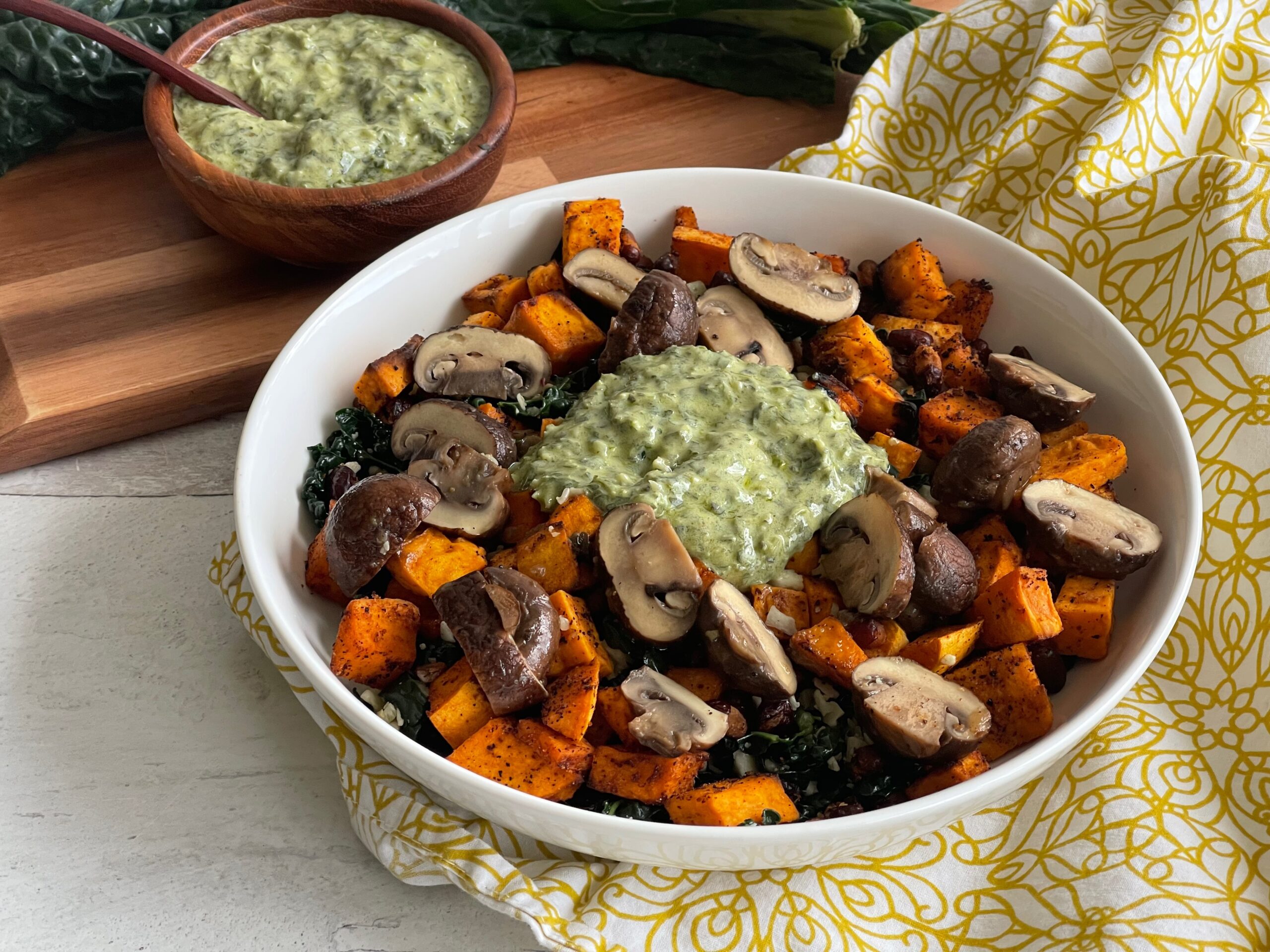 bowl of sweet potatoes and mushrooms with a dollop of green sauce on top next to a smaller bowl of the same green sauce