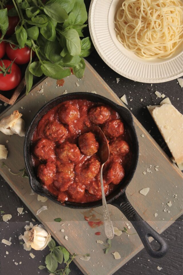 Skillet with Italian meatballs next to a bowl of spaghetti